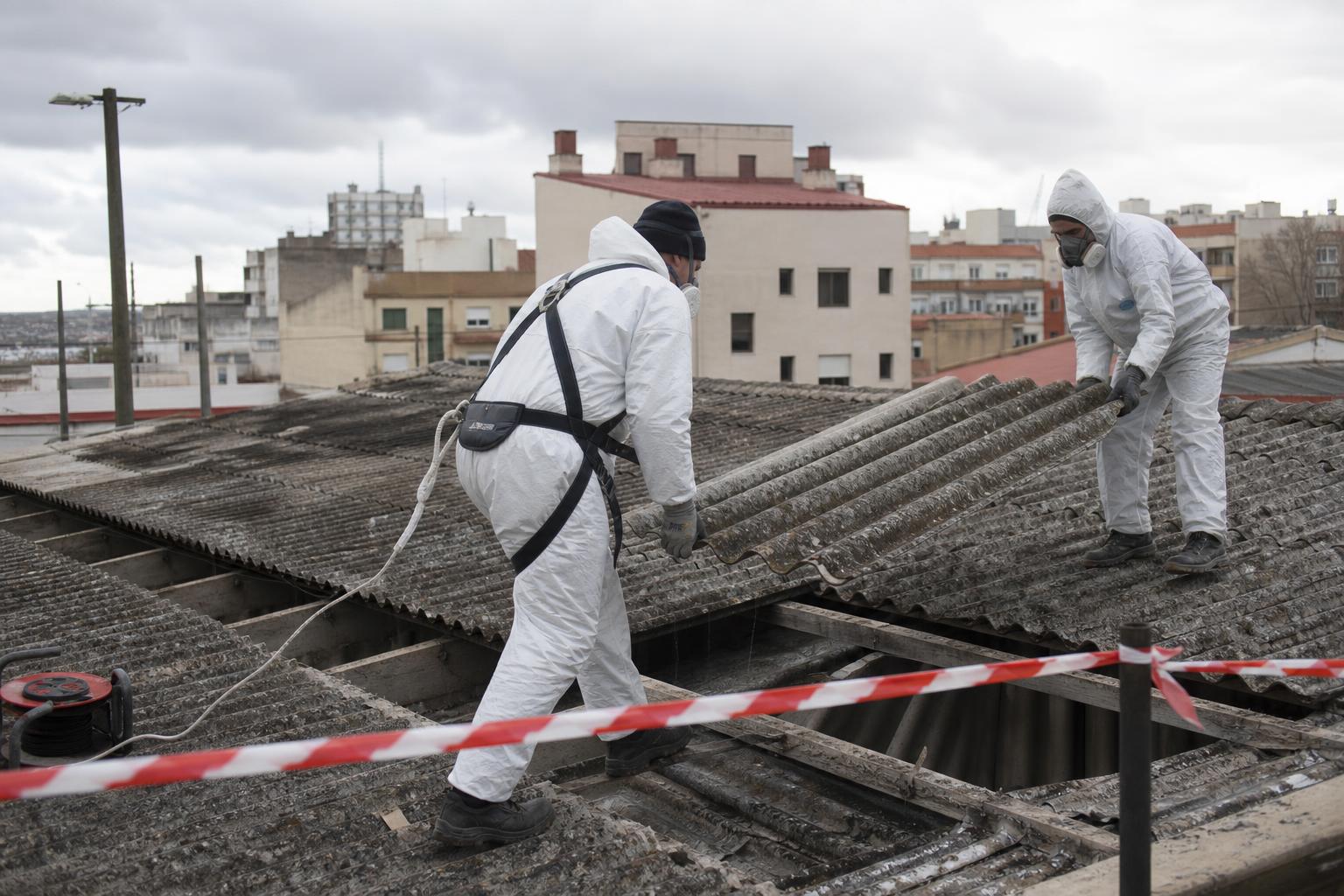 Operarios con equipo de protección retirando placas de fibrocemento con amianto de una cubierta